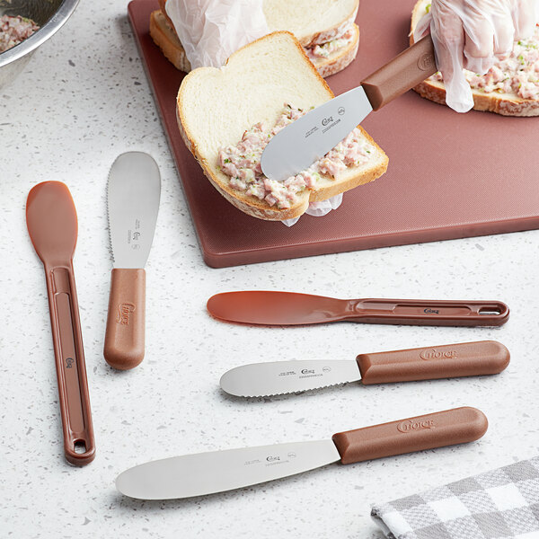 A Choice sandwich spreader with a brown handle spreading food on a piece of bread.