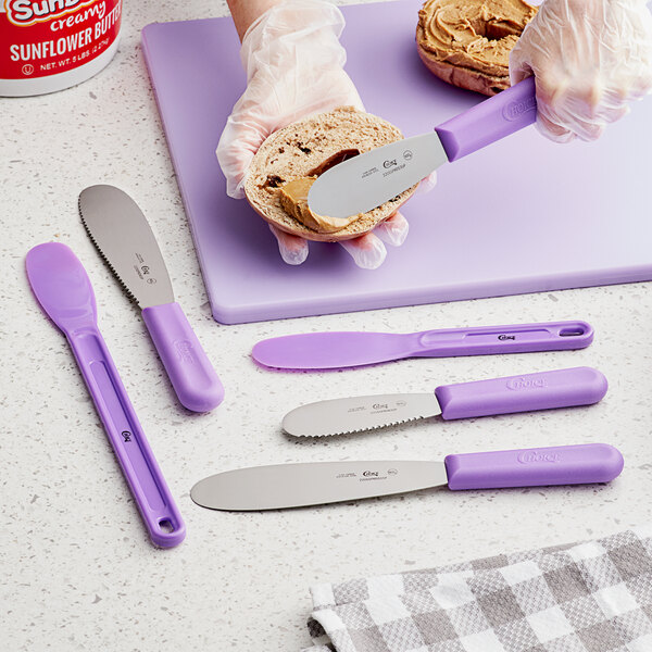 A person's hand spreading a sandwich with a purple Choice sandwich spreader.