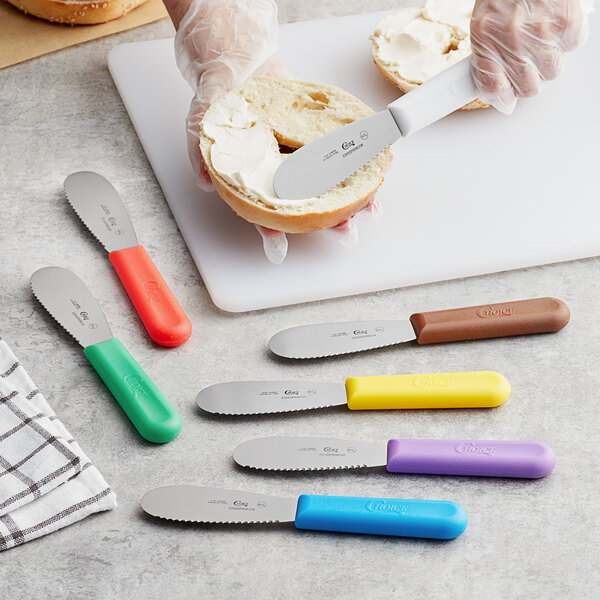 A person spreading butter on a piece of bread with a Choice scalloped sandwich spreader with a blue handle.
