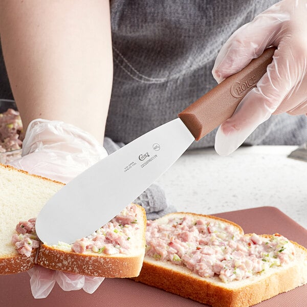 A person spreading meat on a piece of bread with a Choice stainless steel sandwich spreader.