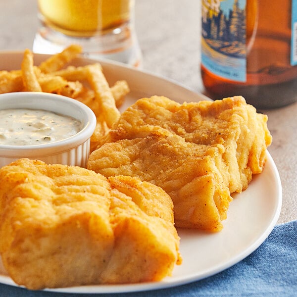 A plate of Zatarain's Seasoned Fish Fri with fries and white sauce next to a glass of beer.
