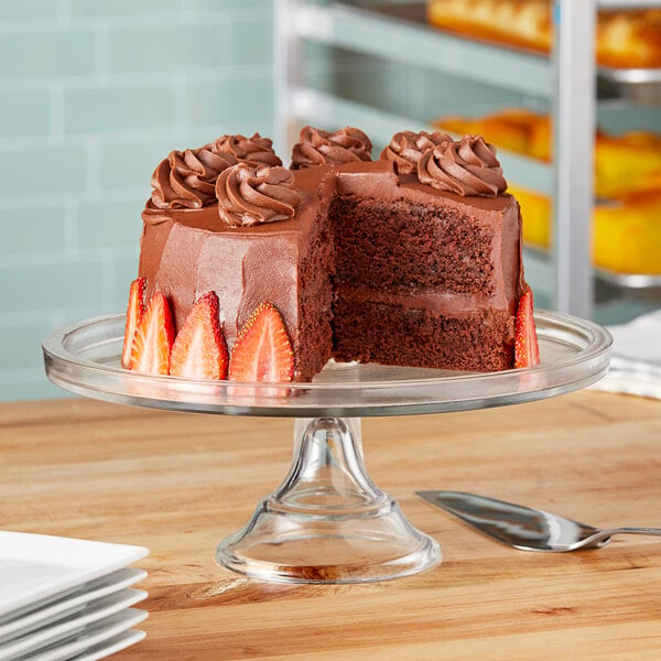 A chocolate cake with frosting and strawberries on a clear glass cake stand.