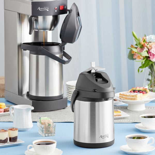 An Avantco stainless steel airpot on a table with cups of coffee.