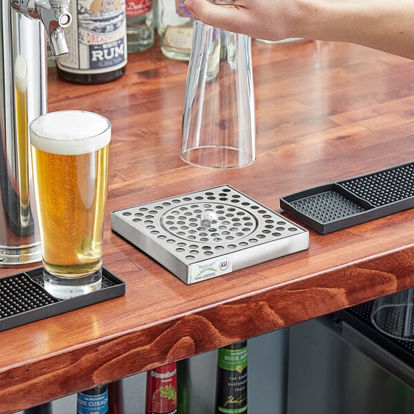 A person using a Regency stainless steel surface mount beer drip tray to pour beer into a glass.