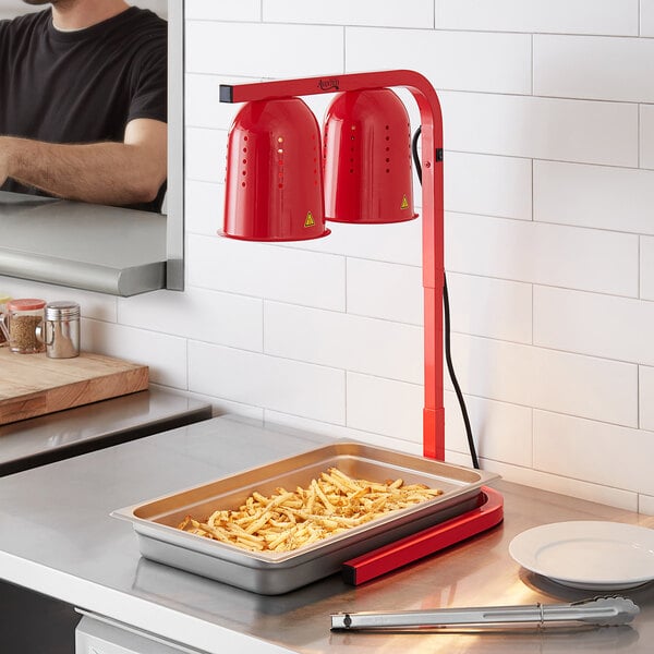 A man using an Avantco red free standing heat lamp to warm a tray of french fries on a counter.