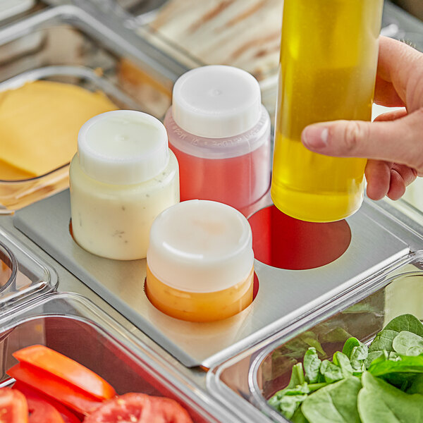 A hand using a Server stainless steel squeeze bottle holder to pour yellow liquid into a container of food.