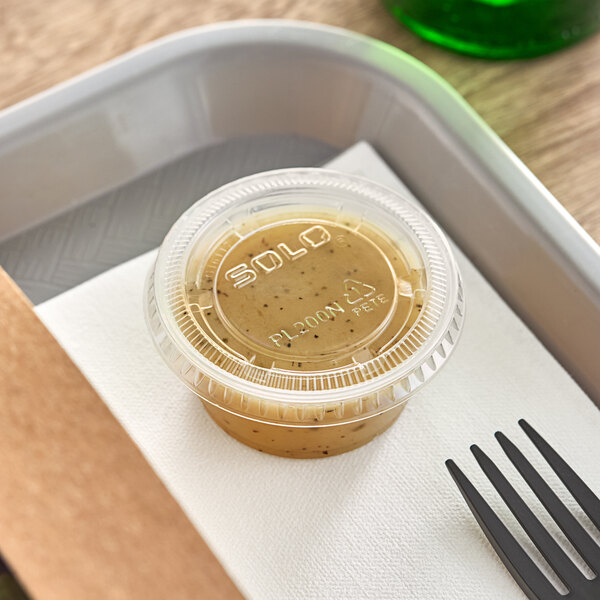 A Solo clear plastic souffle lid on a plastic container of food with a fork.