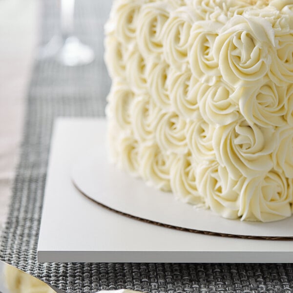 A white square cake on a white melamine-coated wood cake board with feet.