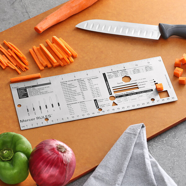 A Mercer Rules Spanish reference tool on a cutting board with vegetables and a knife.