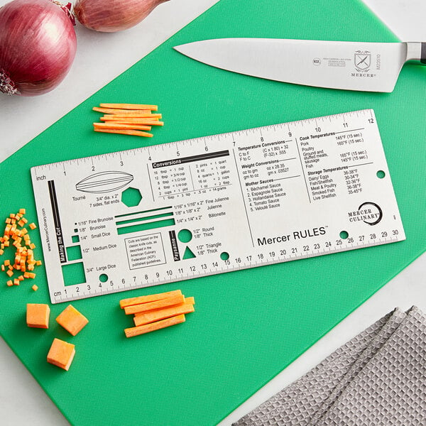 A white rectangular Mercer Rules reference tool with a ruler and knife on a green cutting board.