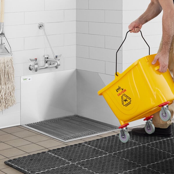 A person using a yellow bucket to fill a Regency stainless steel mop sink.