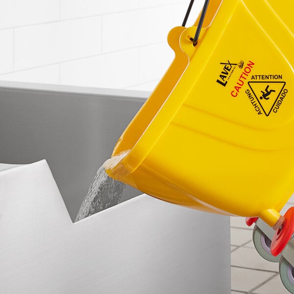 A yellow bucket pouring water into a Regency stainless steel mop sink.