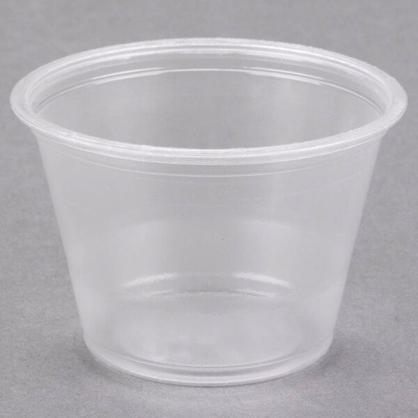 A Dart clear plastic souffle cup with a lid on a grey surface.