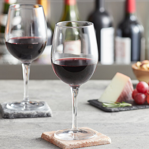 A Pasabahce Moda wine glass filled with red wine on a table with grapes and cheese.