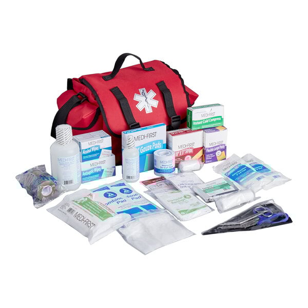 A red trauma first aid kit bag with various medical supplies including bandages, gauze pads, wipes, and scissors displayed in front.