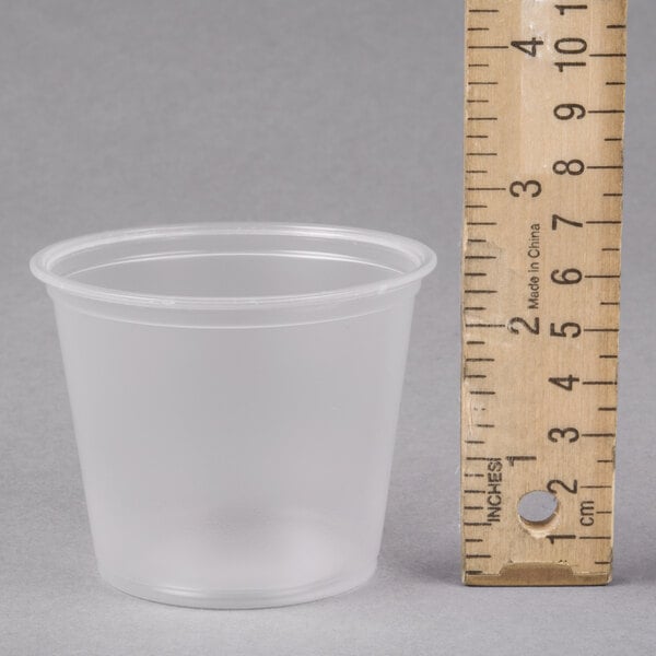 A Dart clear plastic souffle cup on a grey surface with a ruler.