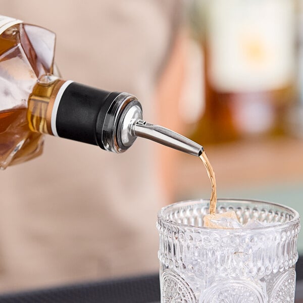 A person using a Carlisle Chrome-Plated Liquor Pourer to pour a drink into a glass with ice.