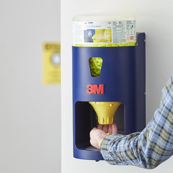 A person filling a blue and yellow 3M E-A-R One Touch earplug dispenser using a yellow and blue container.