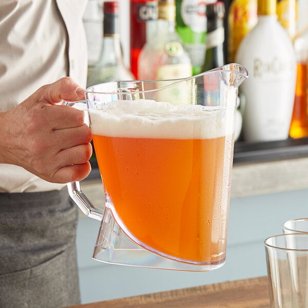 A person holding a San Jamar Perfect Pour plastic beer pitcher filled with orange liquid.