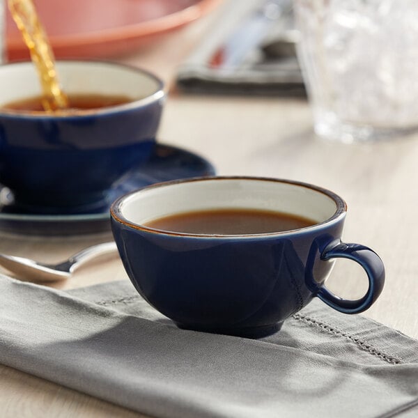 A blue Acopa Keystone stoneware cup filled with brown liquid on a table.