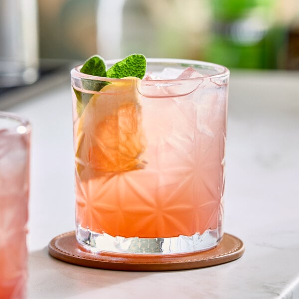 A pink beverage with ice, a citrus slice, and mint leaves served in an 11 oz. Acopa Gardenia rocks glass.
