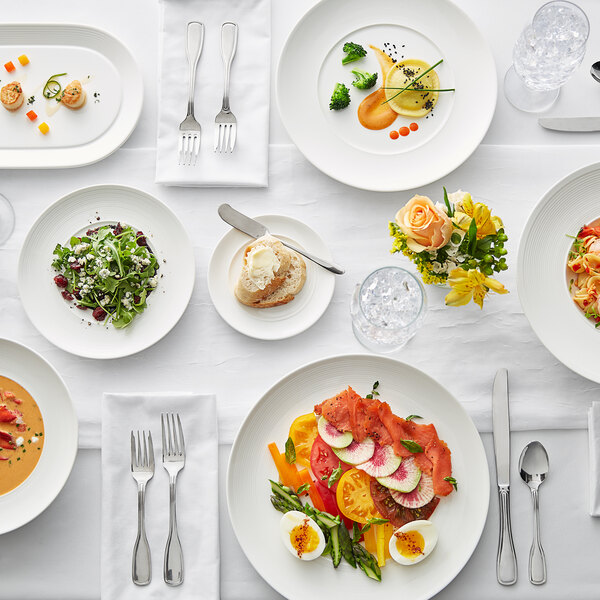 A white table set with an Acopa Liana porcelain plate, food, and silverware.