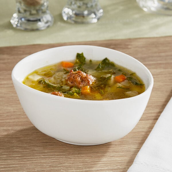 An Acopa Nova cream white stoneware bowl filled with bouillon on a table.