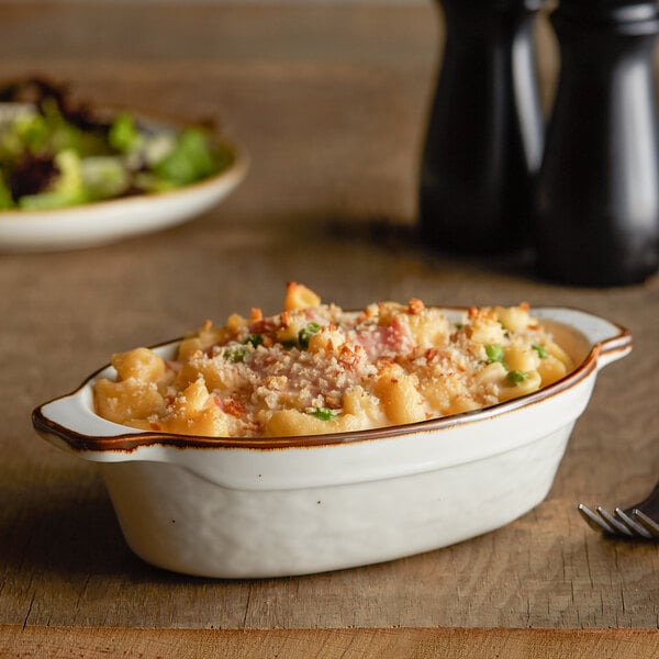 An Acopa Keystone vanilla bean oval casserole dish filled with macaroni and cheese on a table.