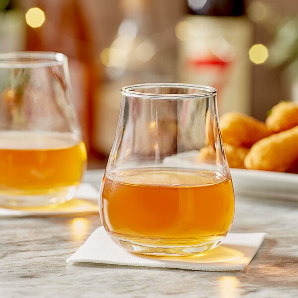 Two Acopa Select whiskey glasses filled with brown liquid on a table next to food