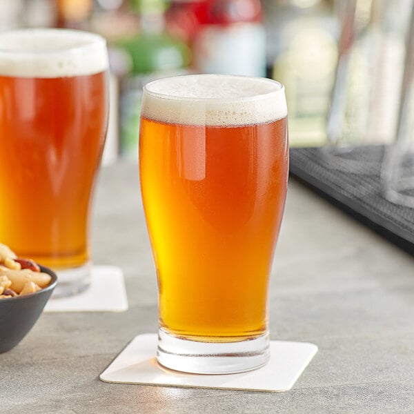 Two Acopa pub glasses of beer on a table with a bowl of nuts.