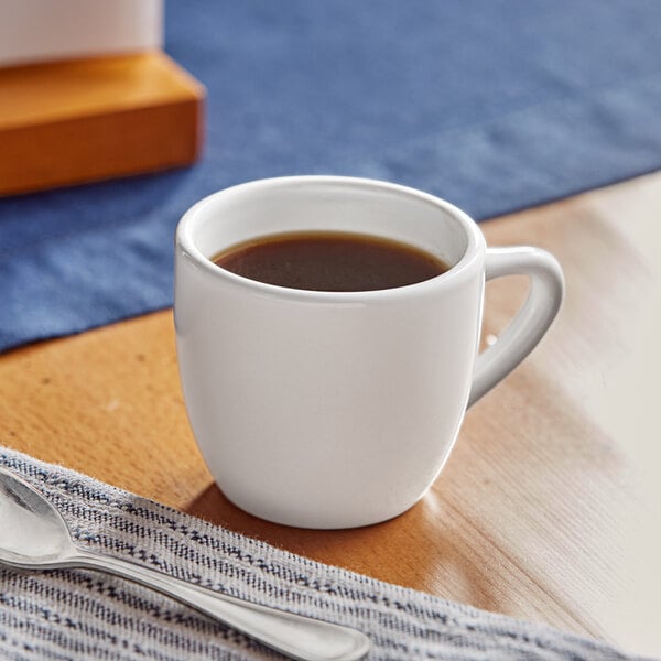 An Acopa bright white stoneware espresso cup on a table with a cup of coffee.
