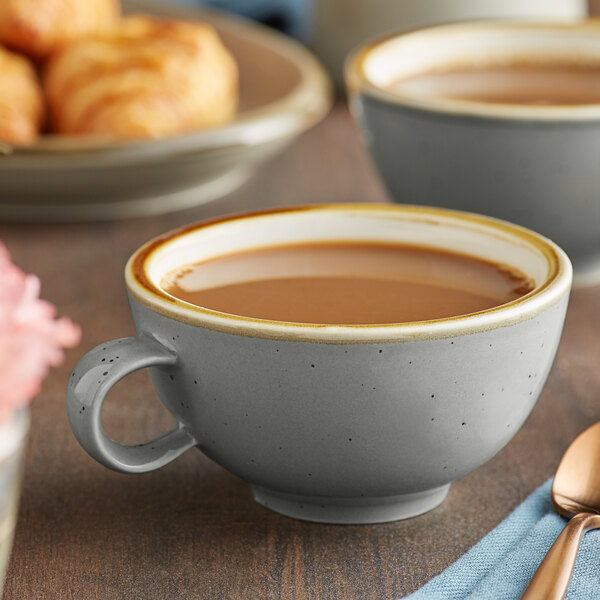 Two Acopa Keystone granite gray stoneware cups of coffee on a table with a spoon and fork.