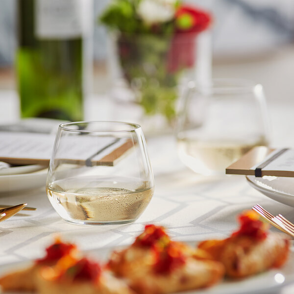 An Acopa Radiance stemless wine glass filled with white wine on a table with food.