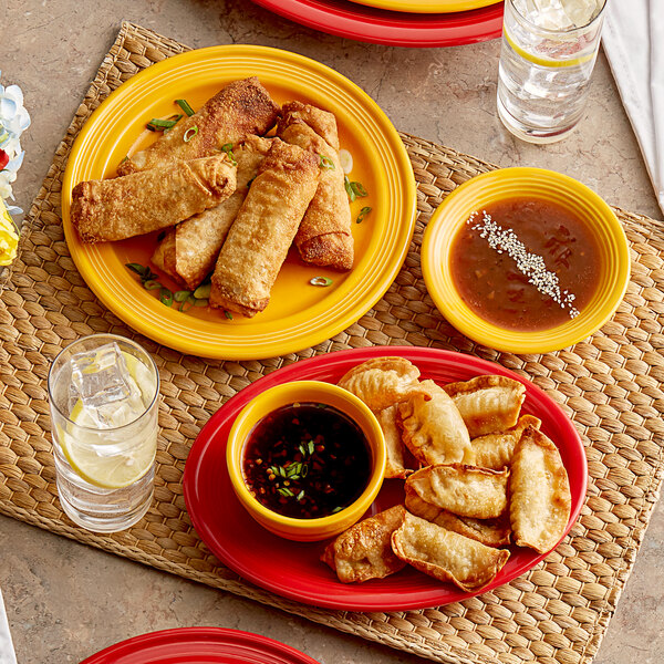 A table with a plate of fried spring rolls, fried dumplings, and a bowl of soup on a Capri mango orange stoneware plate.