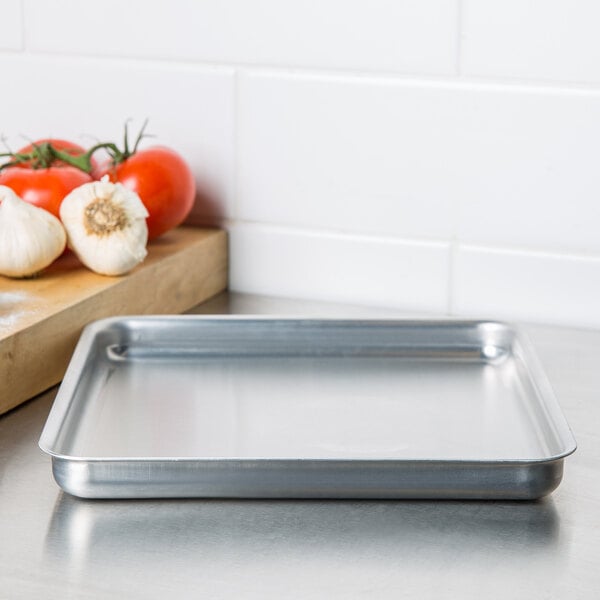 An American Metalcraft aluminum pizza pan on a counter with tomatoes and garlic.