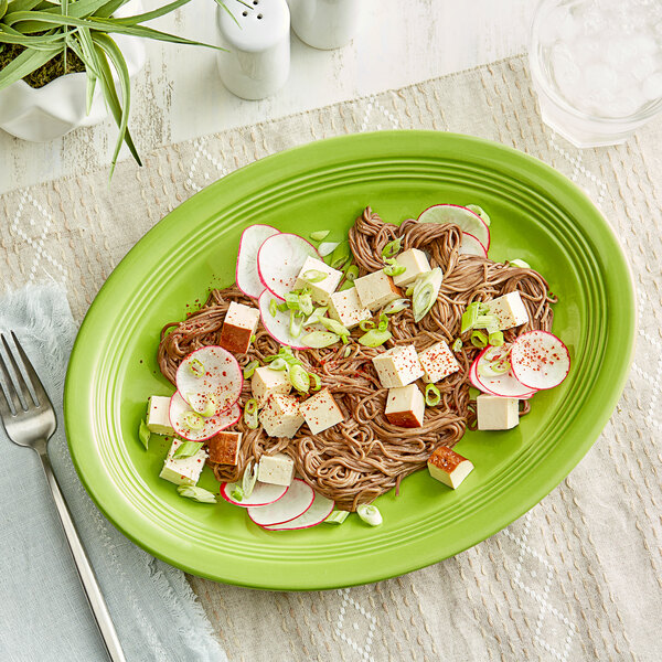 An Acopa Capri bamboo green oval stoneware coupe platter with noodles and vegetables on it.