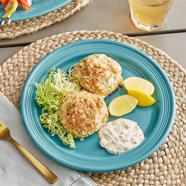 A Capri Caribbean turquoise stoneware plate with crab cakes and a lemon slice on it.