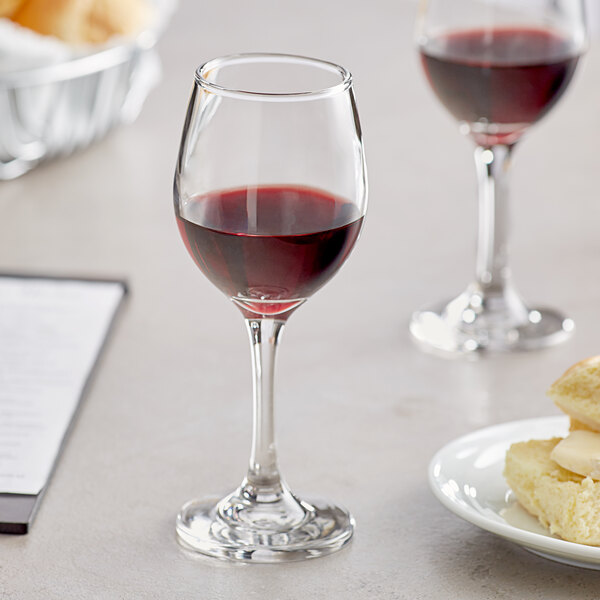 An Acopa all-purpose wine glass filled with red wine next to a plate of food on a white table.