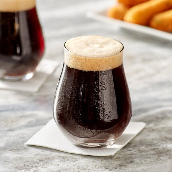 Two Acopa Select stemless tulip glasses of dark beer on a table in a bar with food.