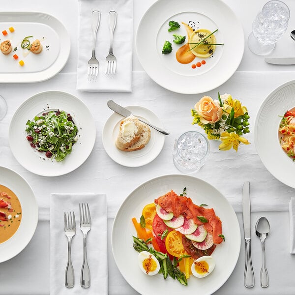 A table set with an Acopa Liana bright white porcelain plate, food, and silverware.