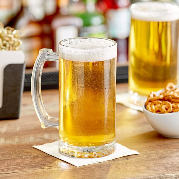An Acopa glass mug of beer on a table with a bowl of pretzels.