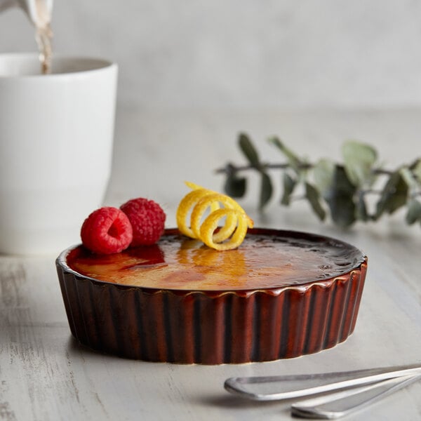 A close up of a dessert with raspberries and lemon in an Acopa Keystone Chestnut souffle dish on a white surface.