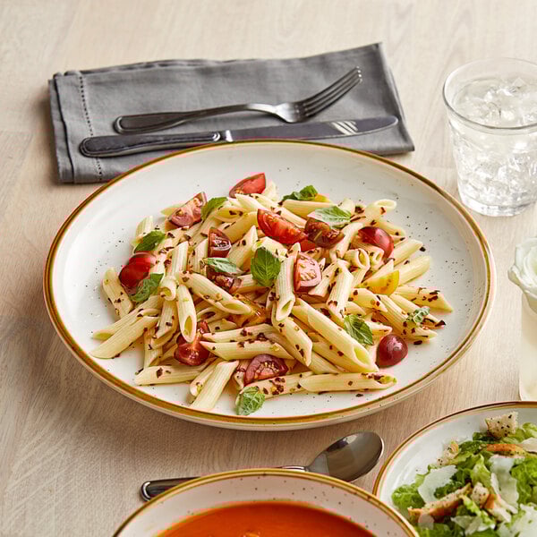 A close up of an Acopa Keystone Vanilla Bean stoneware coupe plate with pasta and salad on it.