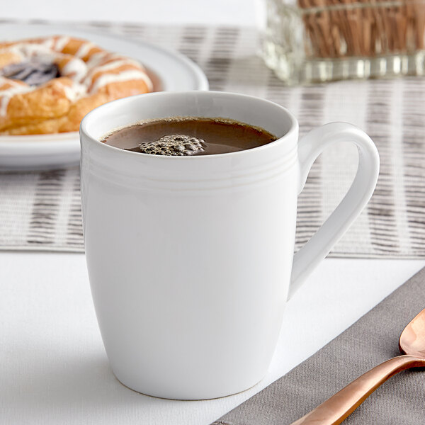 A close-up of an Acopa Capri Coconut White China Mug with brown liquid in it.