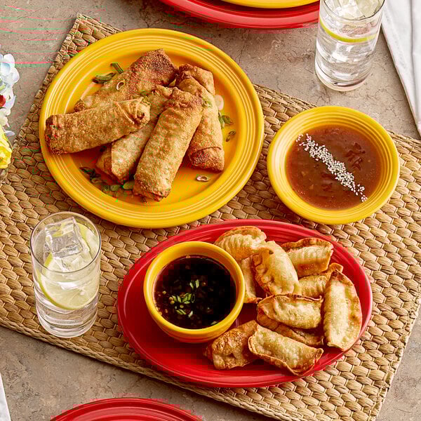 An Acopa Capri passion fruit red oval stoneware platter with fried spring rolls and dumplings on a table with a glass of water.