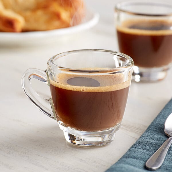 A close-up of two Acopa espresso cups on a table with a glass of coffee.