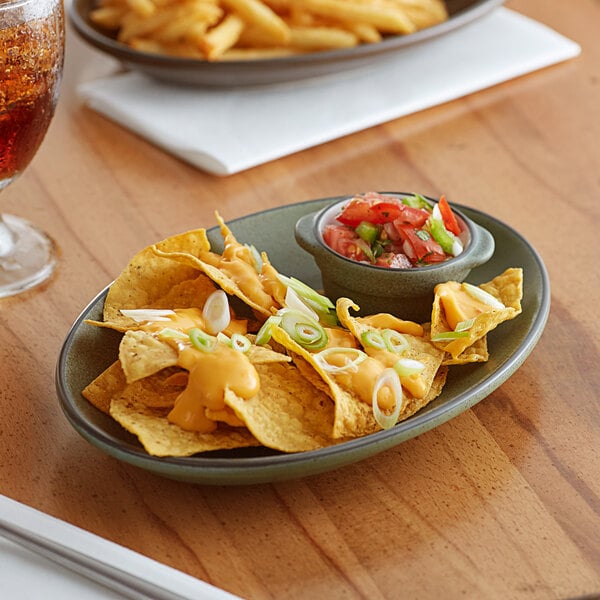 A moss green Acopa stoneware platter with nachos, salsa, and a drink.