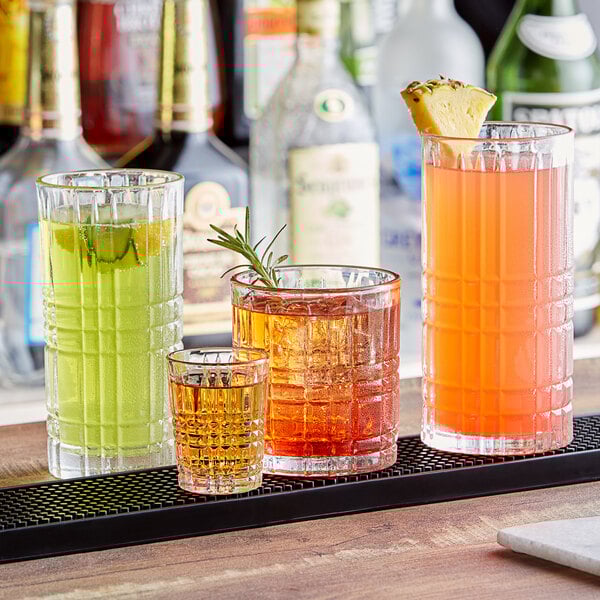 A row of Acopa Madras rocks glasses filled with different colored drinks on a bar.