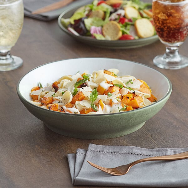 A bowl of pasta in an Acopa moss green stoneware bowl on a table with salad and a glass of wine.