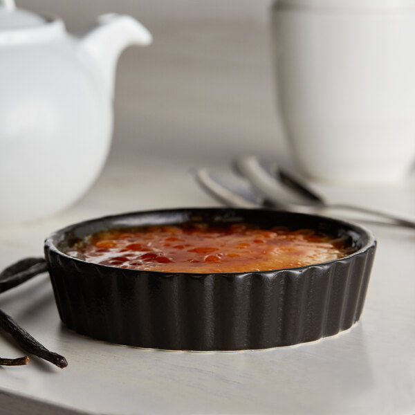 A close up of an Acopa Keystone black stoneware dish filled with orange sauce and vanilla pods.